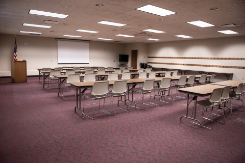 Large meeting room with rows of tables and chairs facing a podium and screen